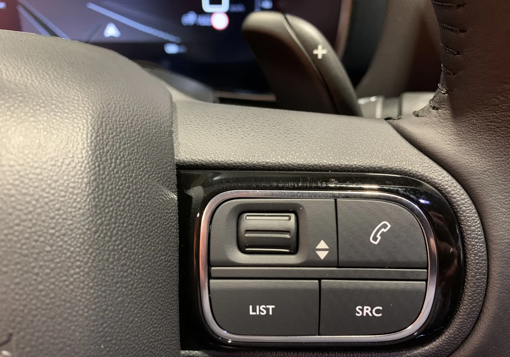 Gros plan sur les commandes du volant noir du Citroën C5 Aircross hybride 2024, boutons de liste et appel visibles.