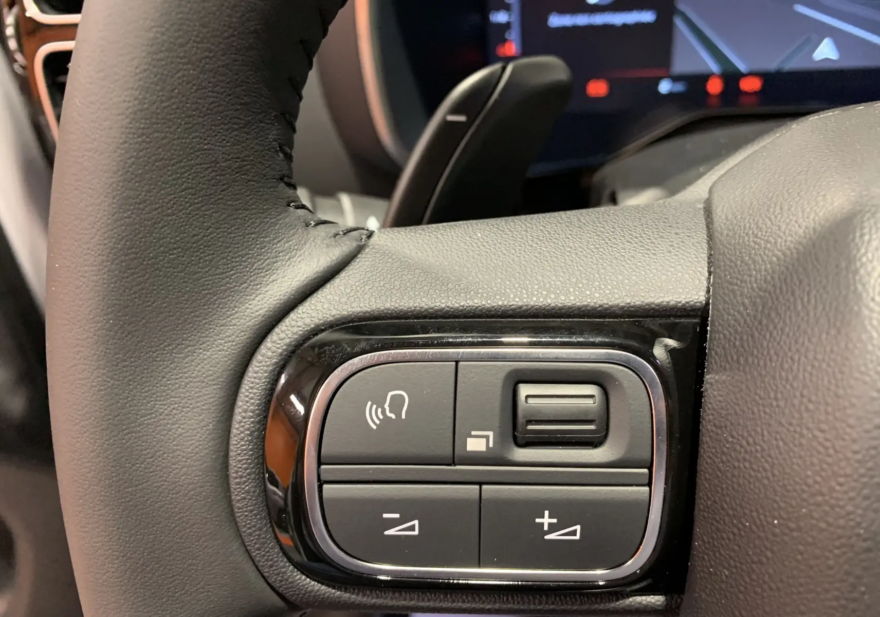 Gros plan sur les commandes du volant noir du Citroën C5 Aircross hybride blanc, avec boutons de volume et reconnaissance vocale.