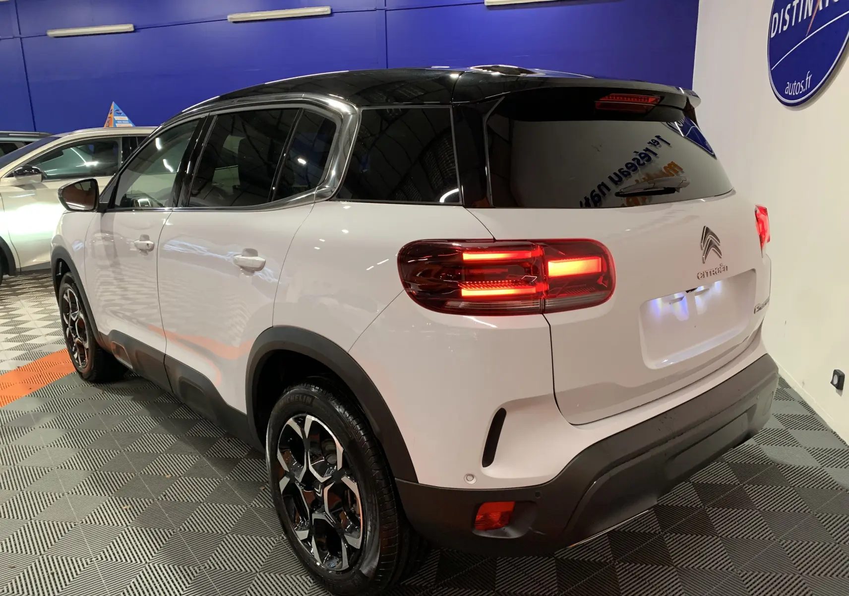 Vue 3/4 arrière droite d'un Citroën C5 Aircross hybride blanc avec toit noir et feux arrière allumés en intérieur showroom.