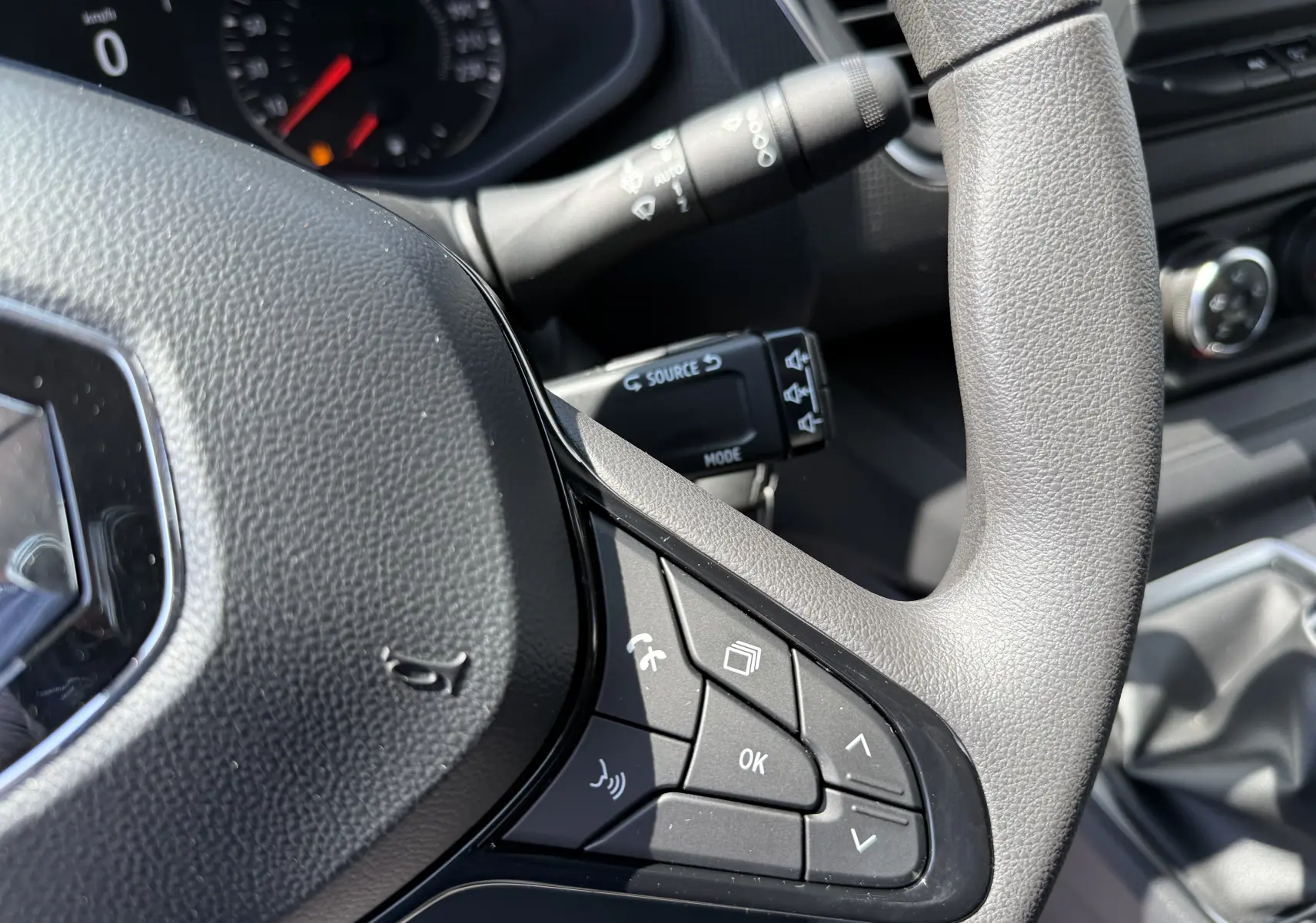 Gros plan sur le volant gris du Renault Trafic Fourgon 2025 avec commandes multifonctions et tableau de bord en arrière-plan.