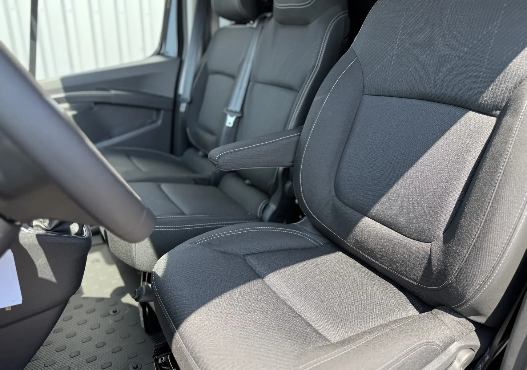Vue rapprochée des sièges avant noirs en tissu du Renault Trafic Fourgon L2H1, avec accoudoir côté conducteur.
