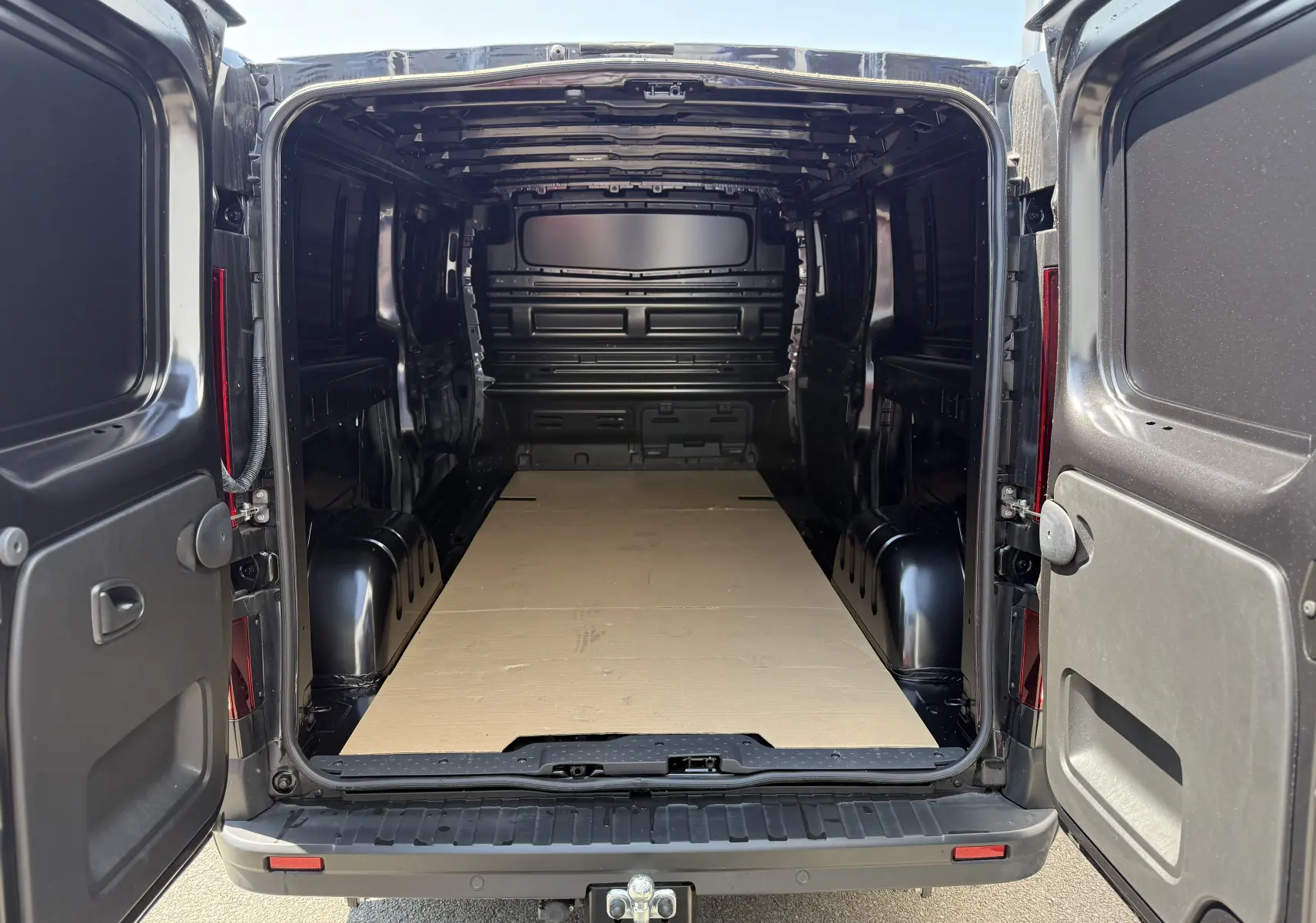 Vue arrière du Renault Trafic Fourgon noir crépuscule métal 2025, portes ouvertes montrant l'espace de chargement vide avec plancher protégé.