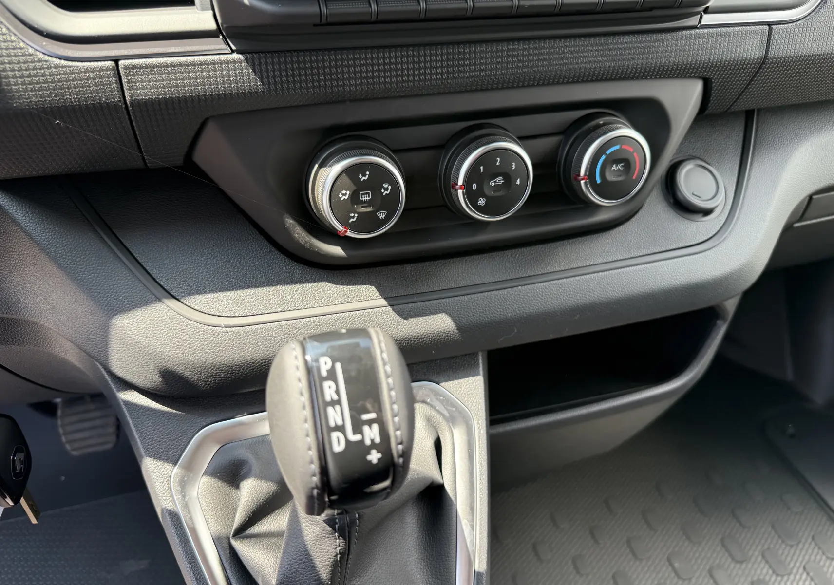 Gros plan sur la console centrale du Renault Trafic Fourgon noir crépuscule, montrant la commande de boîte auto et les réglages climatiques.