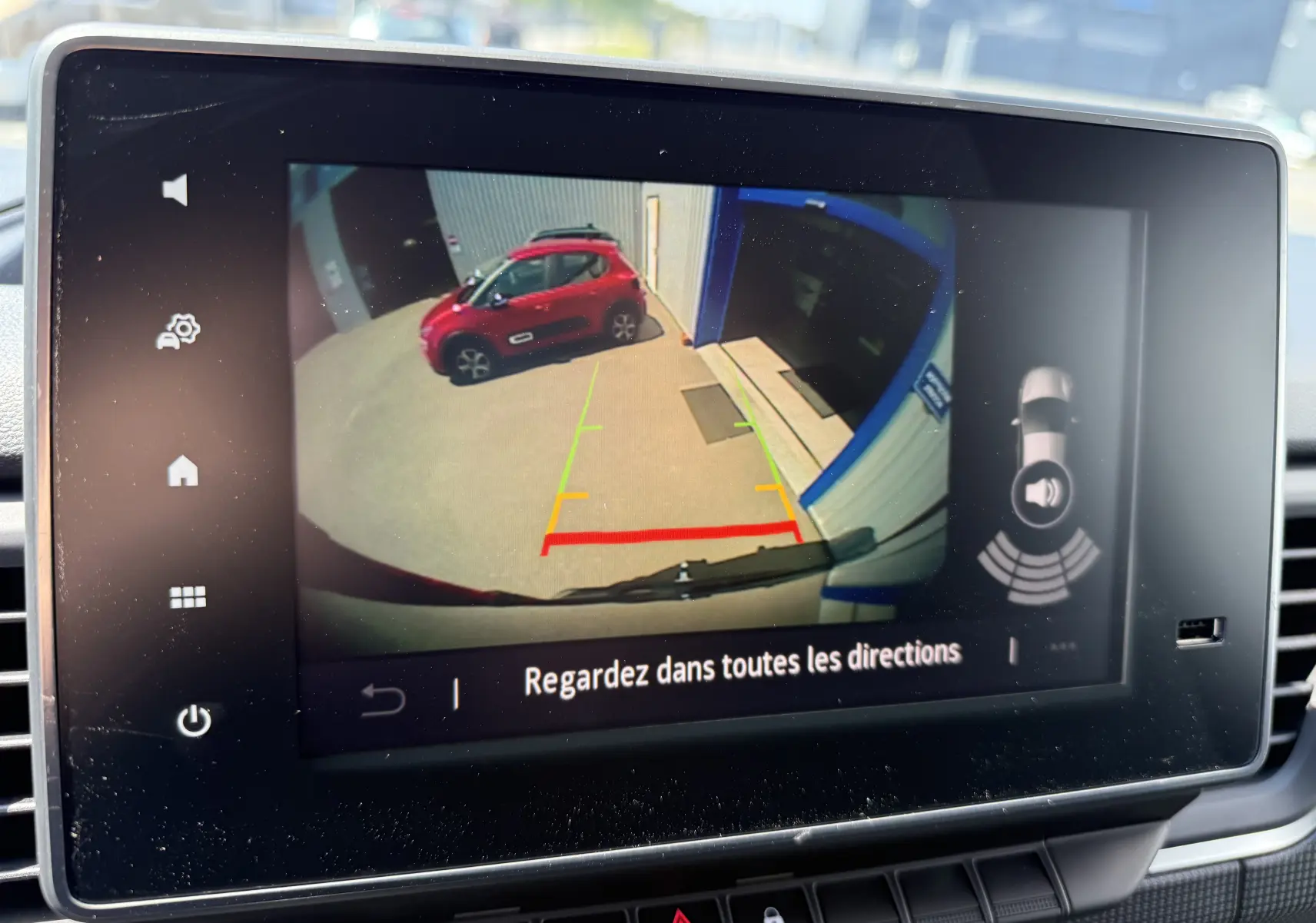 Vue arrière depuis la caméra de recul du Renault Trafic noir crépuscule, avec un véhicule rouge visible à gauche.