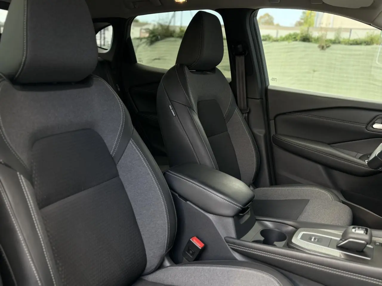 Vue intérieure sur les sièges avant gris et noir du Nissan Qashqai 2025 avec accoudoir central et console moderne.