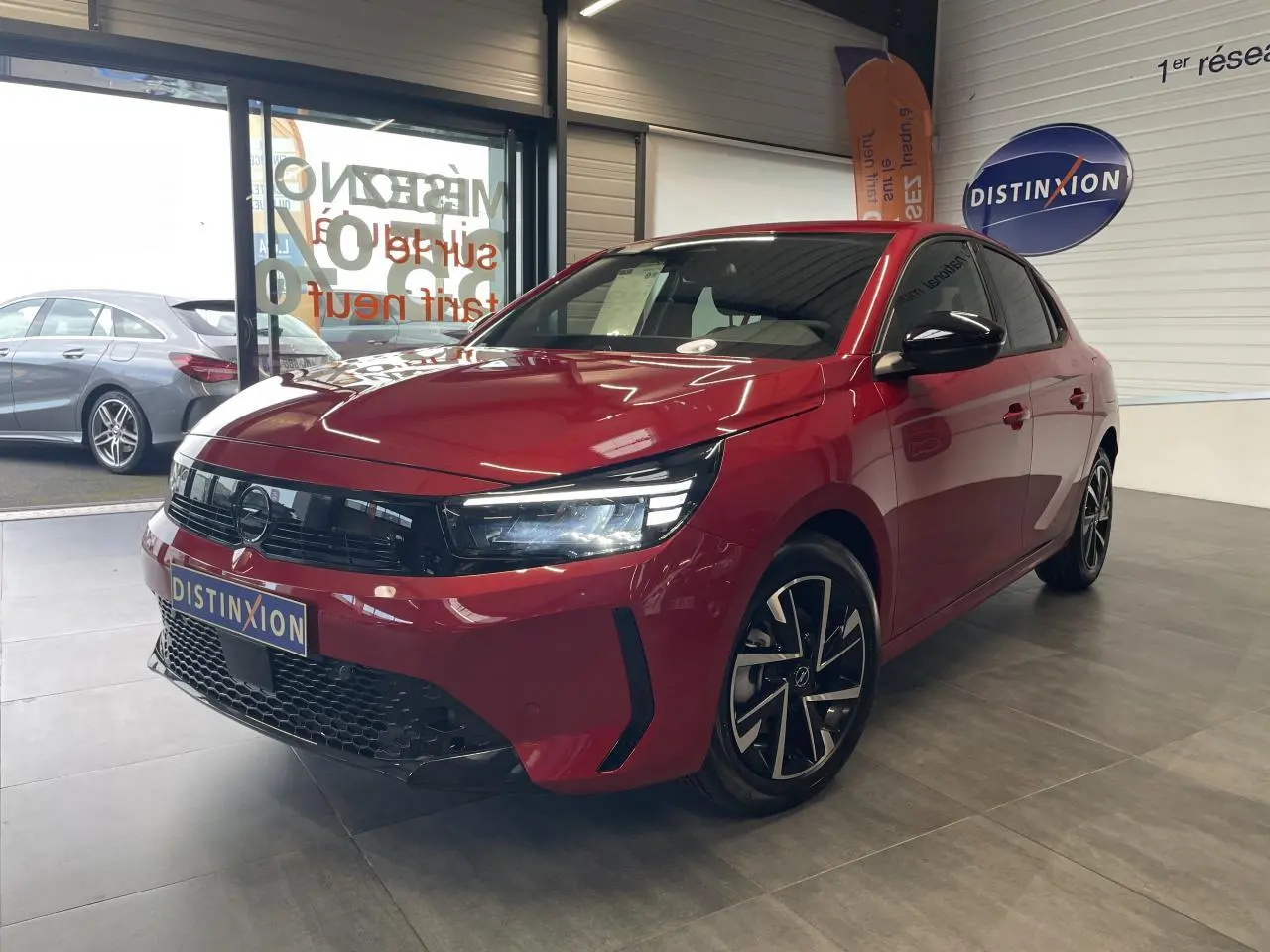 Opel Corsa rouge vue 3/4 avant droit en intérieur, calandre noire et jantes alliage diamantées.