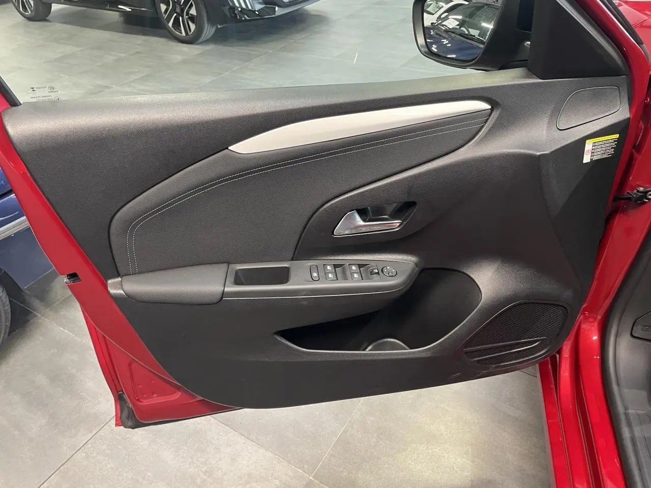 Vue intérieure de la porte avant gauche rouge d'une Opel Corsa 2026 avec commandes électriques et garniture noire.