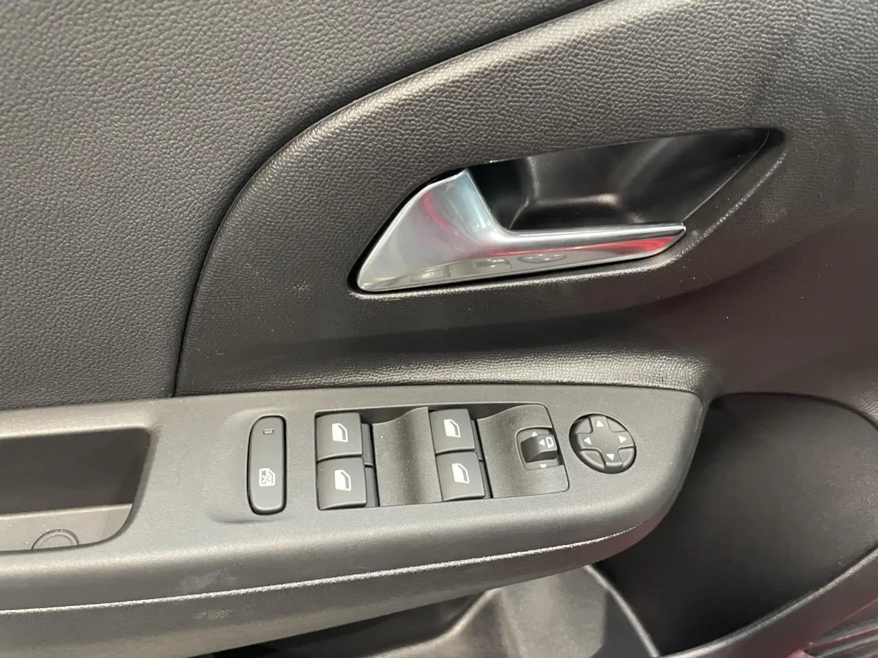 Gros plan sur la commande des vitres et rétroviseurs côté conducteur d'une Opel Corsa rouge, intérieur noir.
