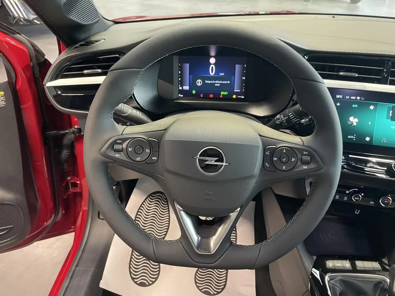 Vue intérieure centrée sur le volant noir de l'Opel Corsa rouge avec tableau de bord numérique et écran tactile.