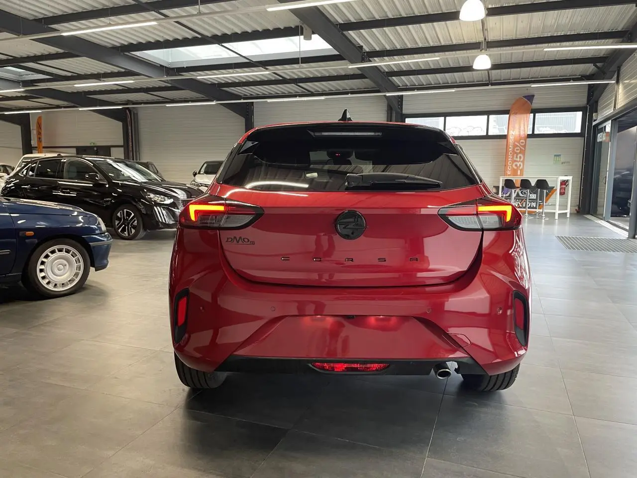 Vue arrière d'une Opel Corsa rouge métallisée avec feux LED et logo noir dans un showroom.