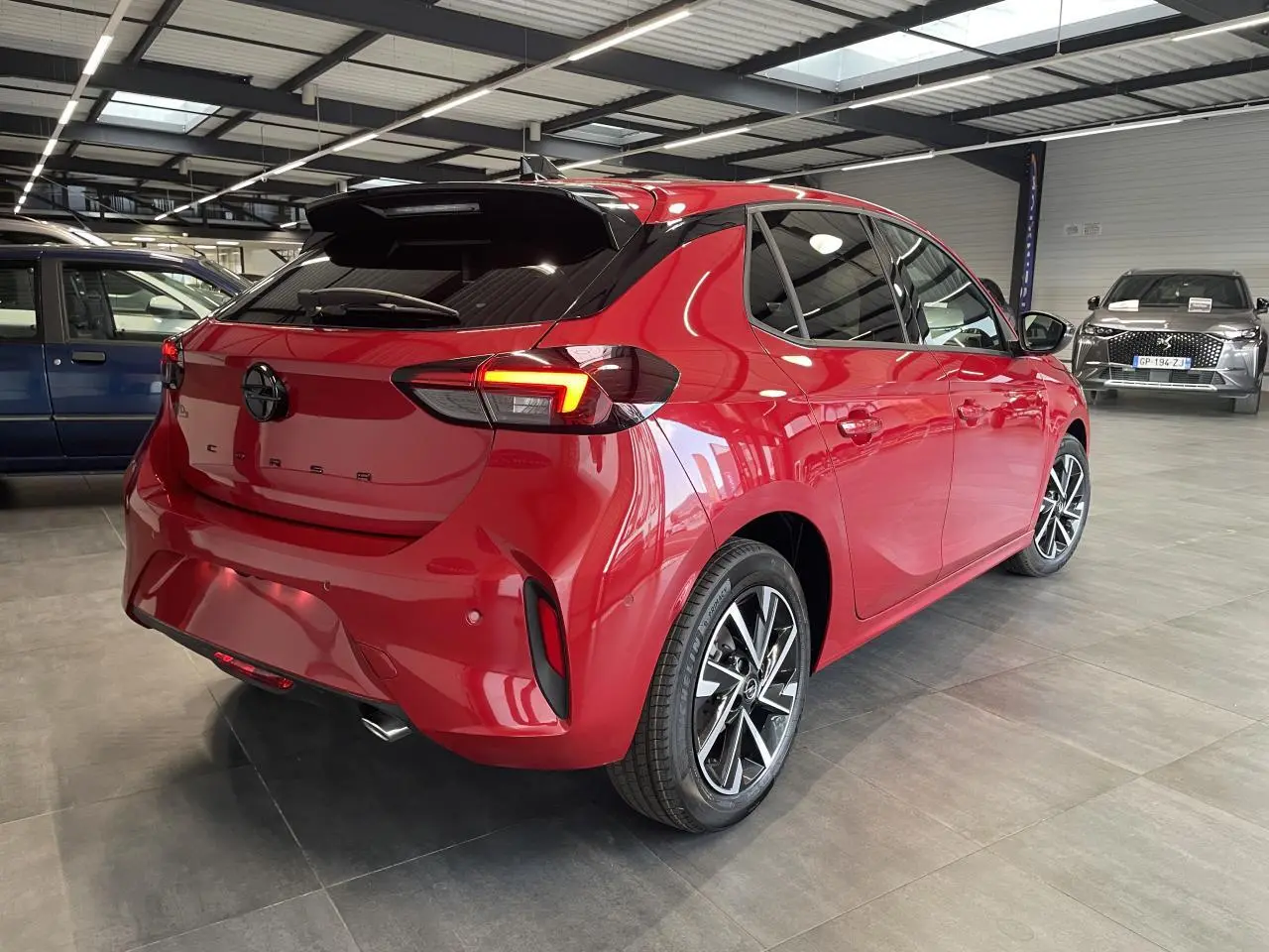 Vue 3/4 arrière droite d'une Opel Corsa rouge métallisée avec jantes alliage et vitres arrière surteintées en showroom.
