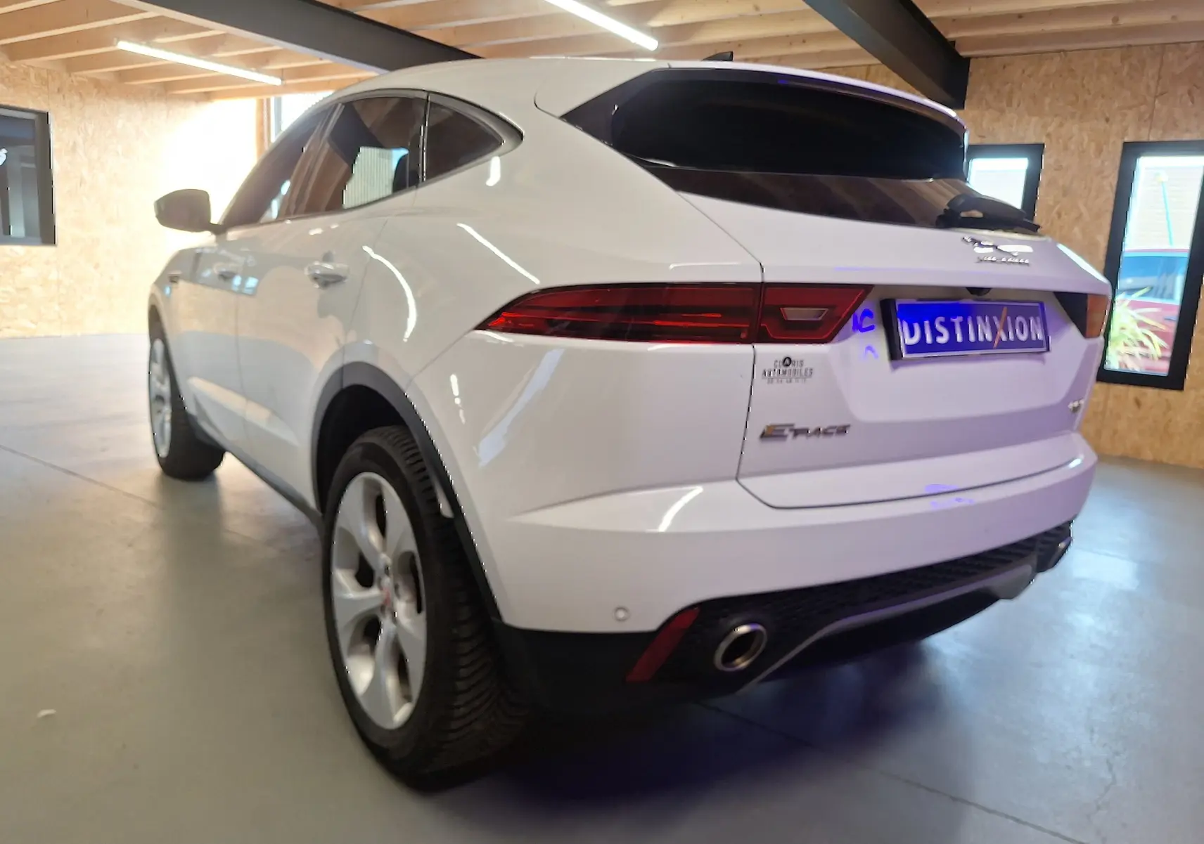 Vue 3/4 arrière gauche d'un Jaguar E-PACE blanc avec feux arrière LED et double sortie d'échappement visible en intérieur.