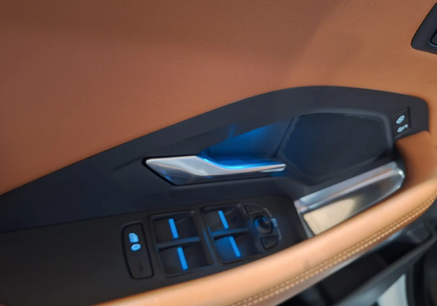 Gros plan sur la garniture intérieure côté conducteur en cuir marron avec commandes électriques et poignée métal du Jaguar E-PACE blanc.