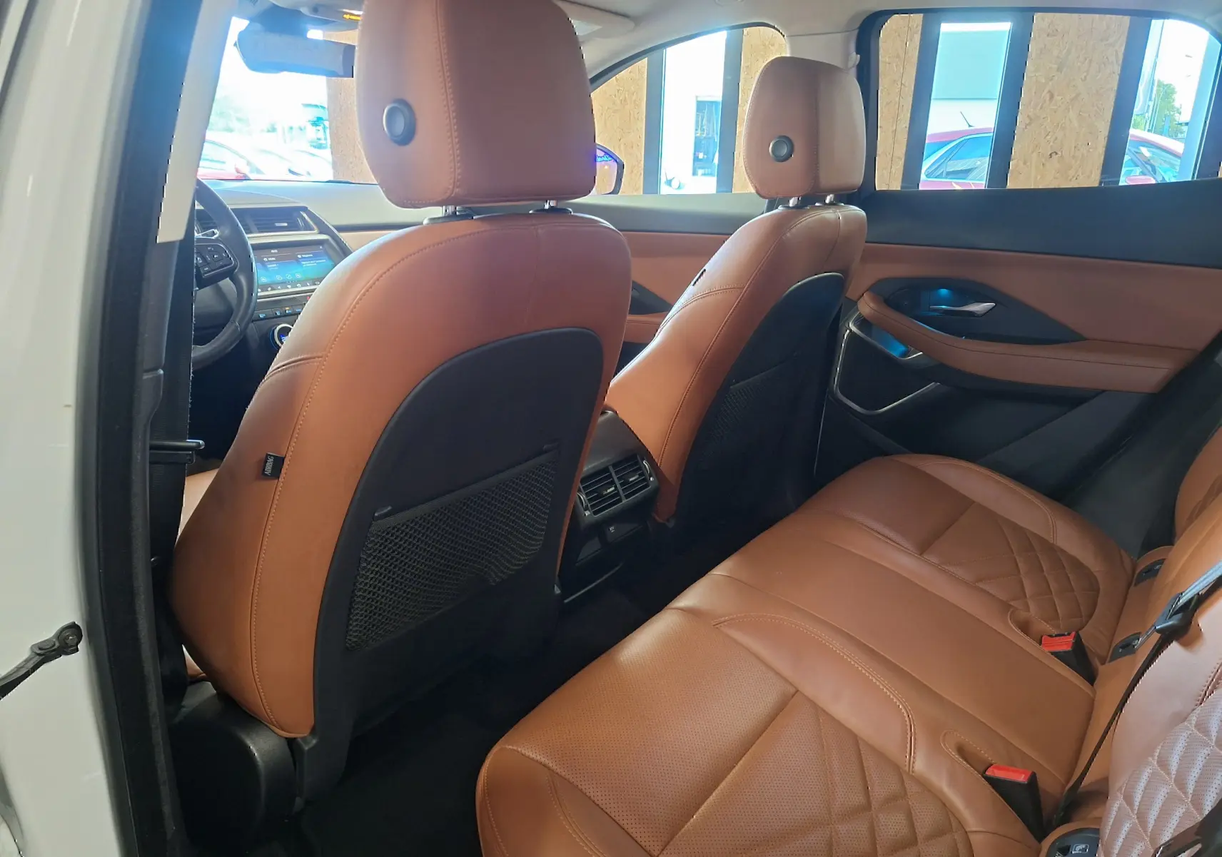 Vue intérieure arrière droite du Jaguar E-PACE blanc 2019, sièges en cuir marron avec surpiqûres et console centrale visible.