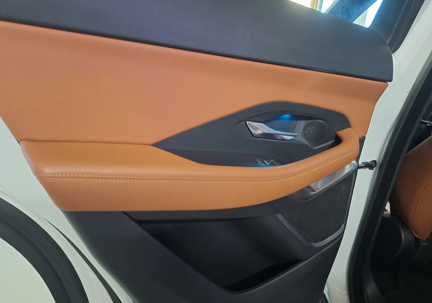 Gros plan sur la porte arrière droite blanche du Jaguar E-PACE 2019 avec garniture cuir marron et détails chromés.