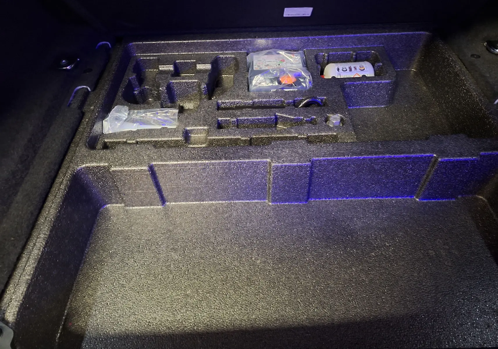 Coffre ouvert du Jaguar E-PACE blanc 2019, vue plongeante sur le rangement en mousse avec outils et accessoires.