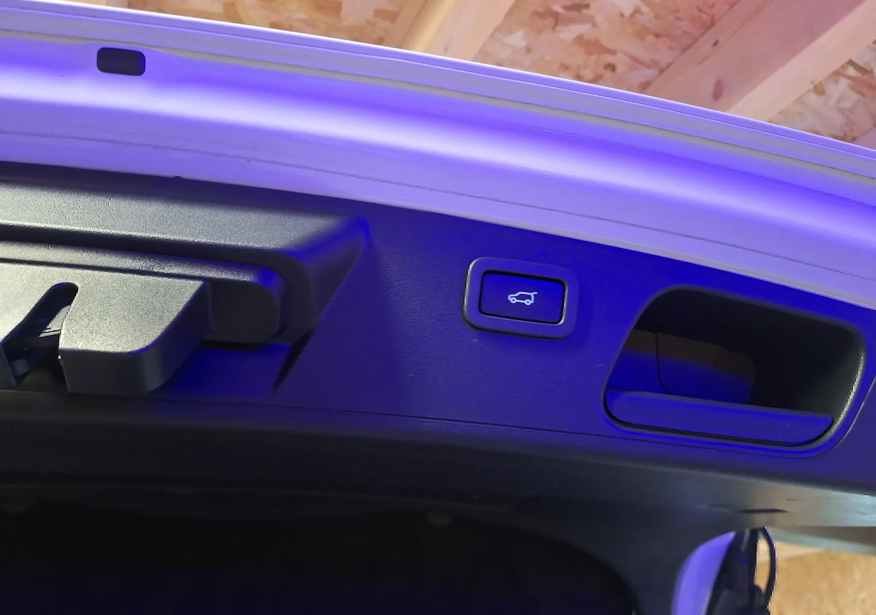 Détail du bouton d'ouverture électrique du coffre sur la partie intérieure du hayon d'un Jaguar E-PACE blanc.