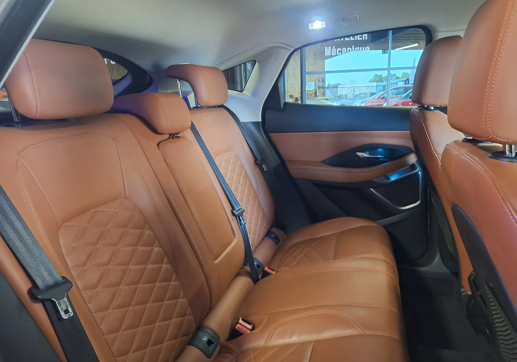 Vue intérieure arrière droite des sièges en cuir marron matelassé du Jaguar E-PACE 2019, ambiance élégante et lumineuse.