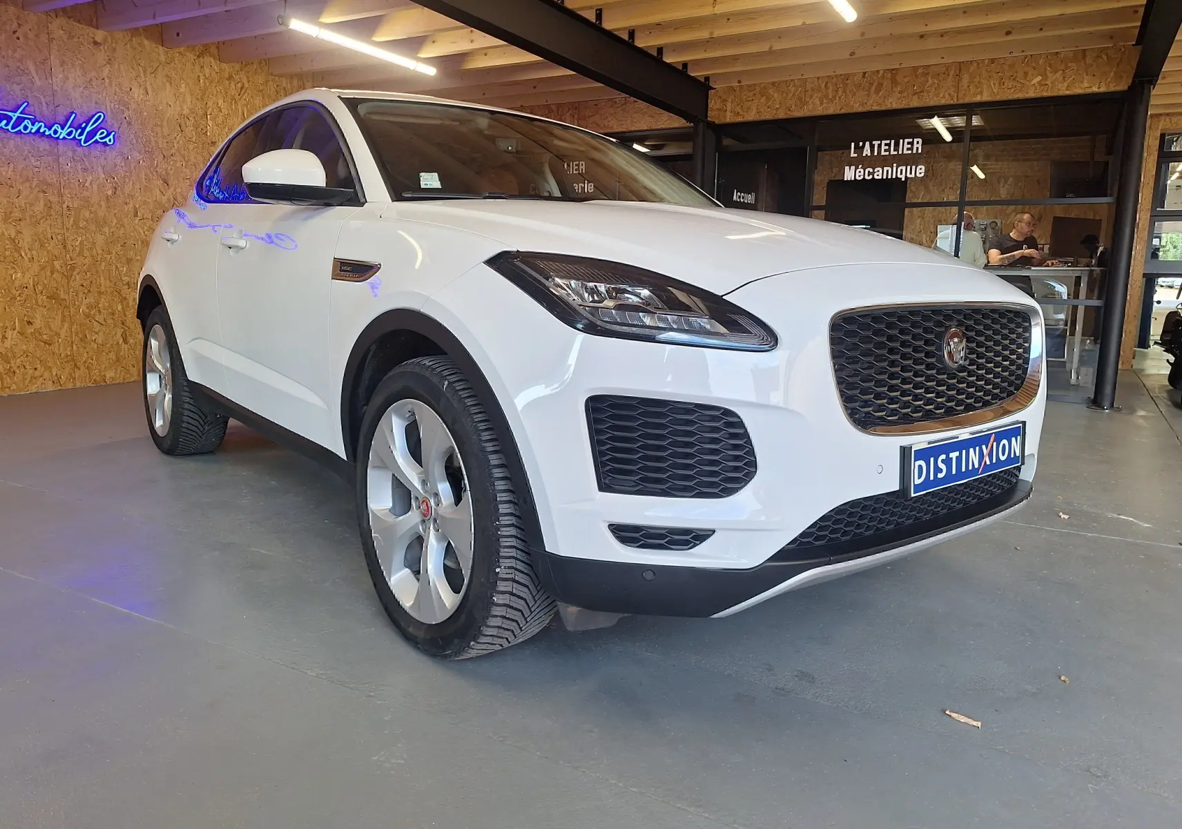 Jaguar E-PACE blanc vue 3/4 avant droit, avec calandre noire et phares LED dans un atelier.