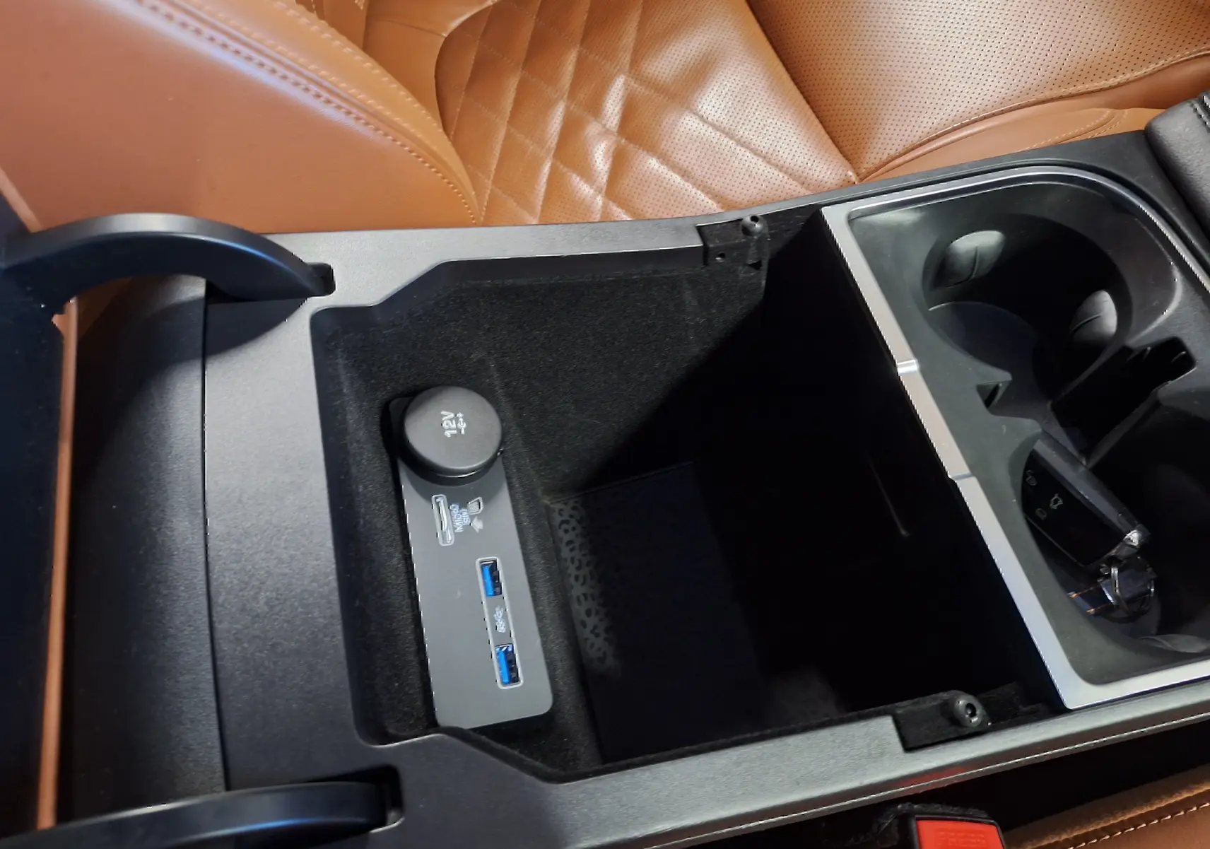 Gros plan intérieur sur la console centrale ouverte avec prises USB et cuir marron du siège Jaguar E-PACE blanc.