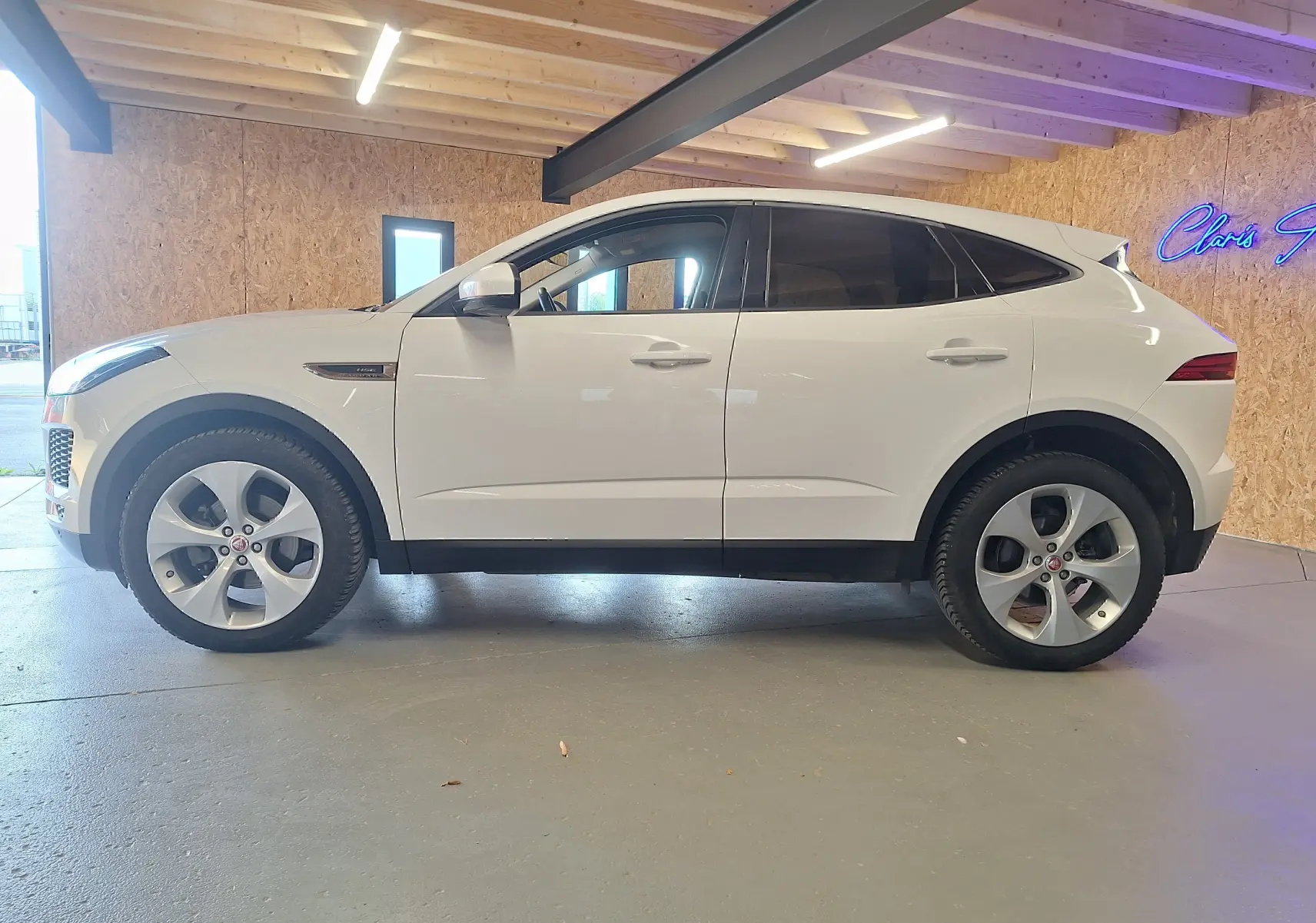 Profil gauche d'un Jaguar E-PACE blanc 2019 avec jantes alliage et rétroviseurs électriques dans un garage.
