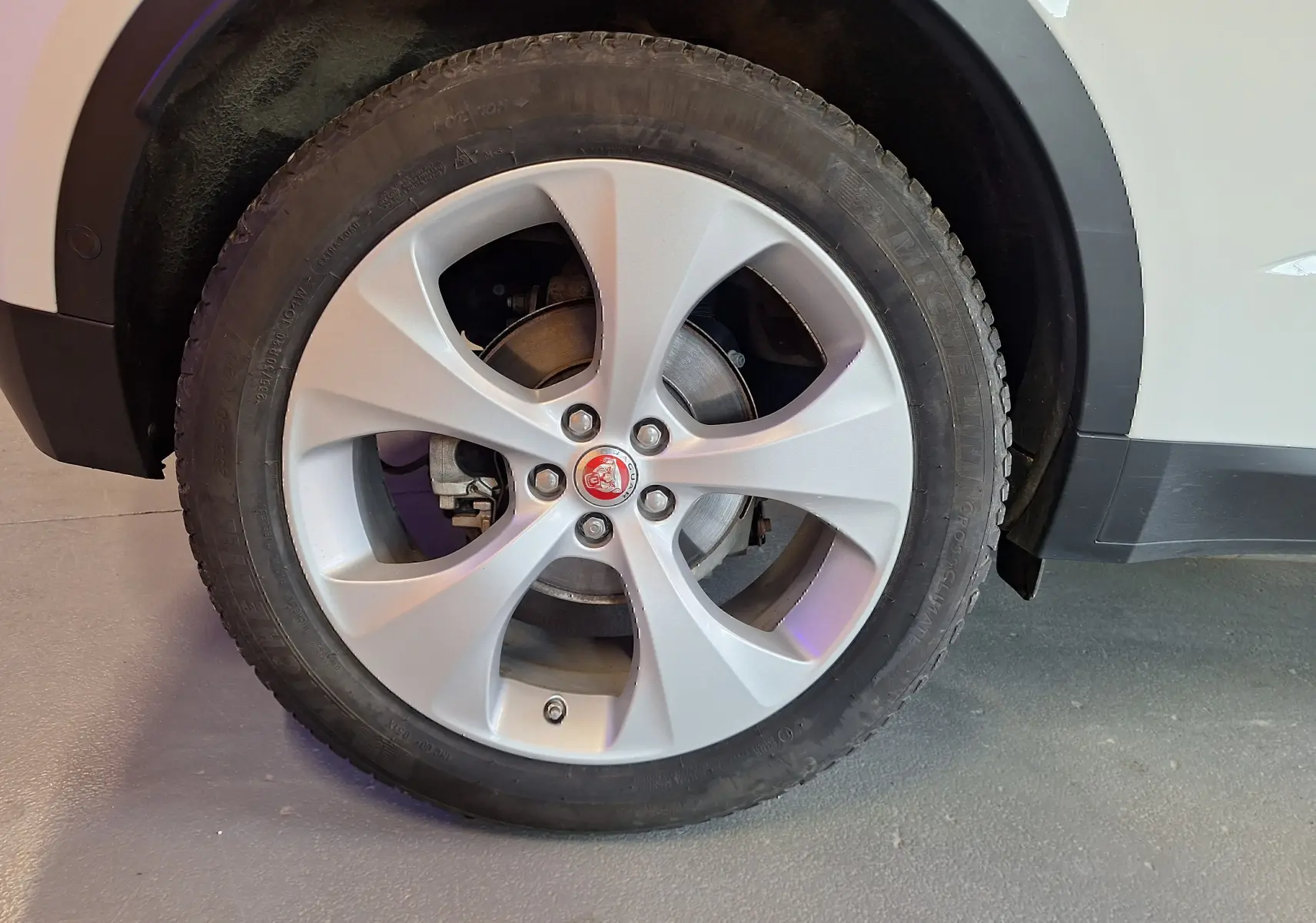 Gros plan sur la roue avant droite argentée avec logo Jaguar sur un Jaguar E-PACE blanc.