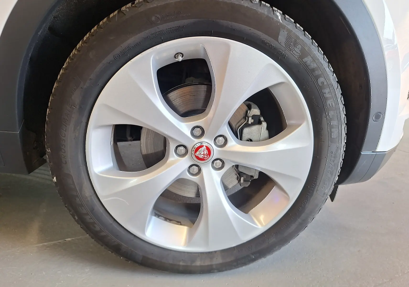 Gros plan sur la roue avant droite blanche d’un Jaguar E-PACE 2.0 D180 R-DYNAMIC HSE avec jante argentée et logo Jaguar rouge.