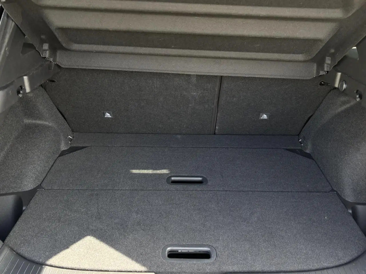 Coffre modulable ouvert du Nissan Qashqai III gris Ceramic, montrant le plancher de coffre plat et les poignées intégrées.