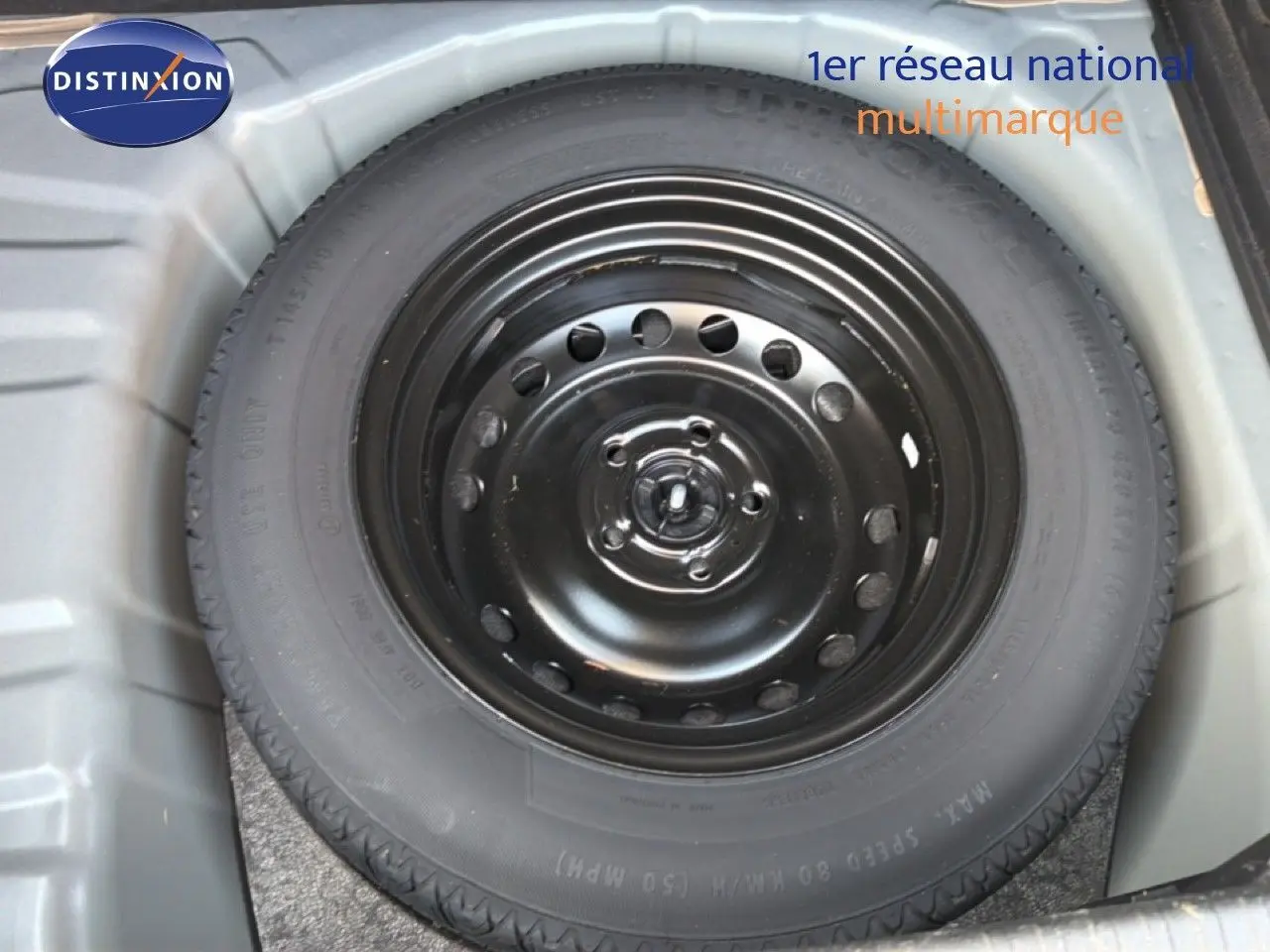 Roue de secours noire dans le coffre d’un Renault Captur bleu marine fumé, vue en plongée.