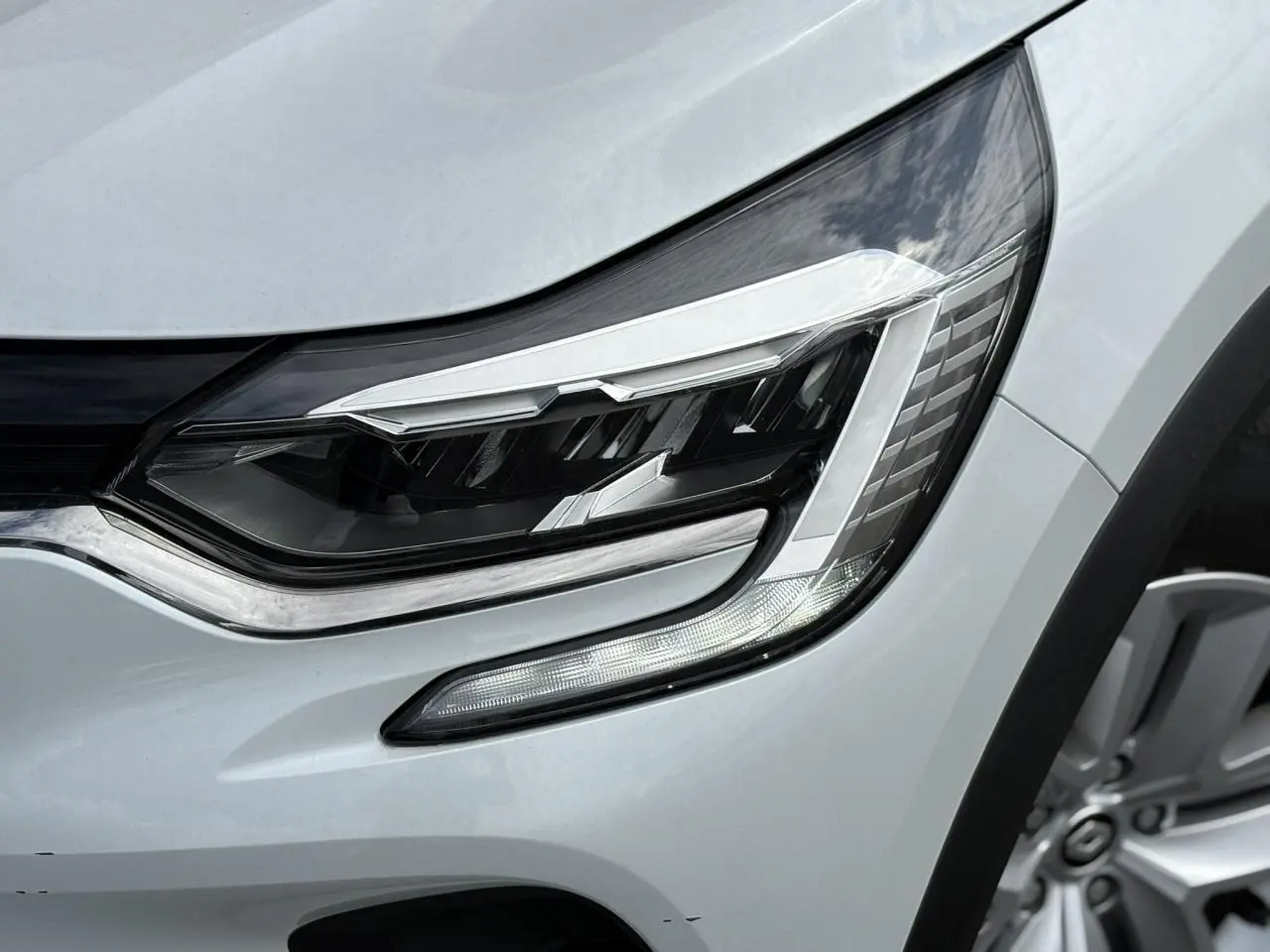 Gros plan sur le phare avant droit du Renault Captur blanc nacré 2022 avec jante alliage visible.