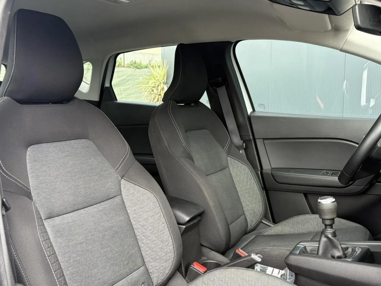 Vue intérieure sur les sièges avant gris et la console centrale avec levier de vitesses manuelle du Renault Captur blanc nacré 2022.