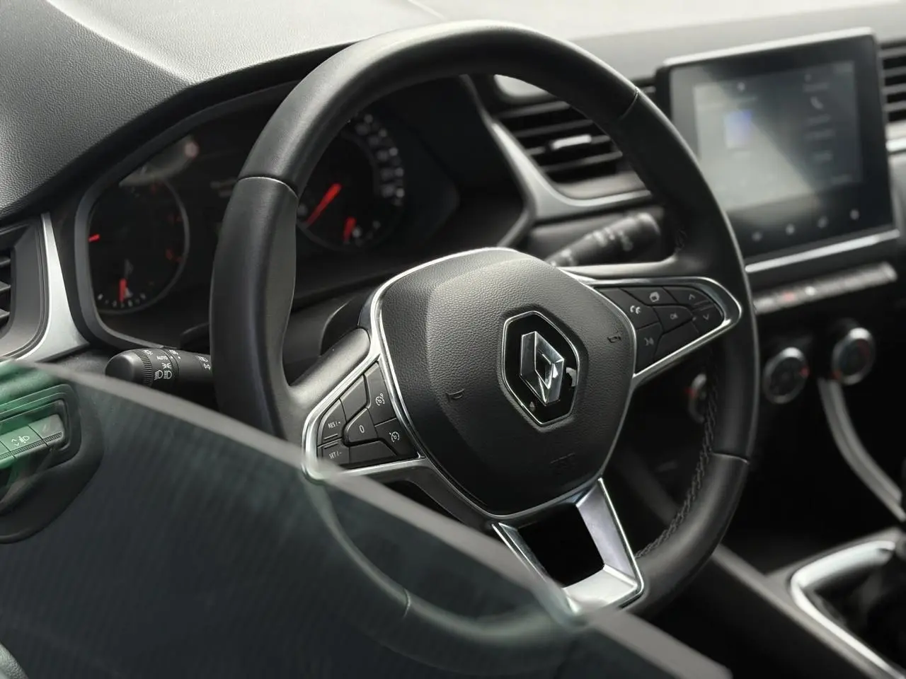 Vue rapprochée du volant noir du Renault Captur 2022 avec commandes intégrées et tableau de bord numérique flou.
