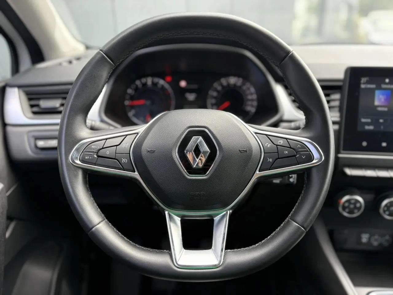 Volant en cuir noir de Renault Captur 2022 avec commandes intégrées et tableau de bord flou en arrière-plan.