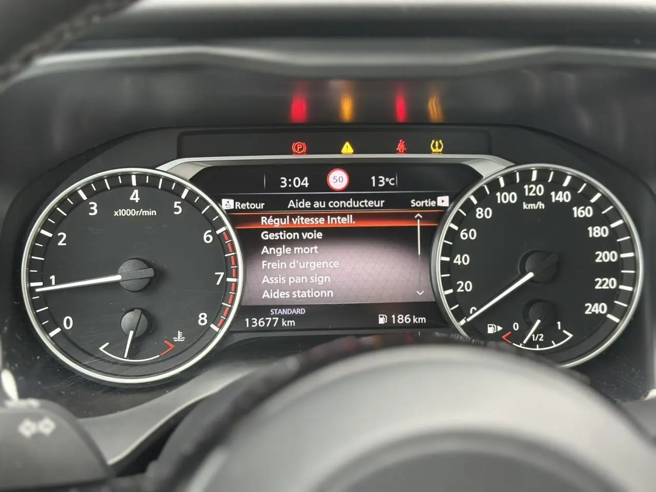 Tableau de bord du Nissan Qashqai 2024 avec compte-tours, vitesse, et écran d'aide au conducteur affichant les alertes.