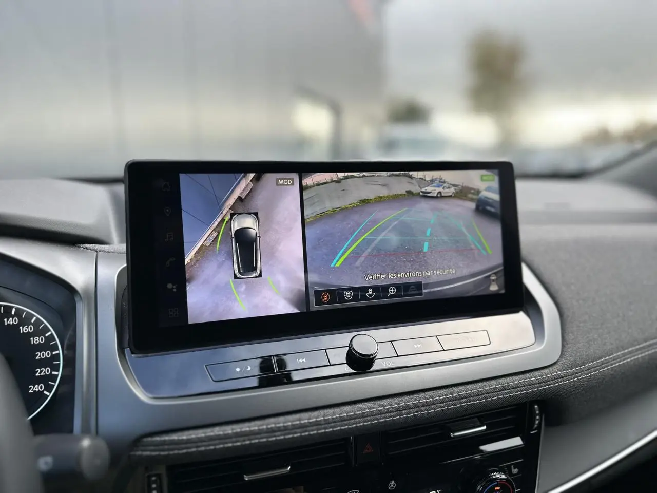 Vue intérieure du tableau de bord du Nissan Qashqai 2024 avec écran tactile affichant la caméra de recul et vue 360° du véhicule.