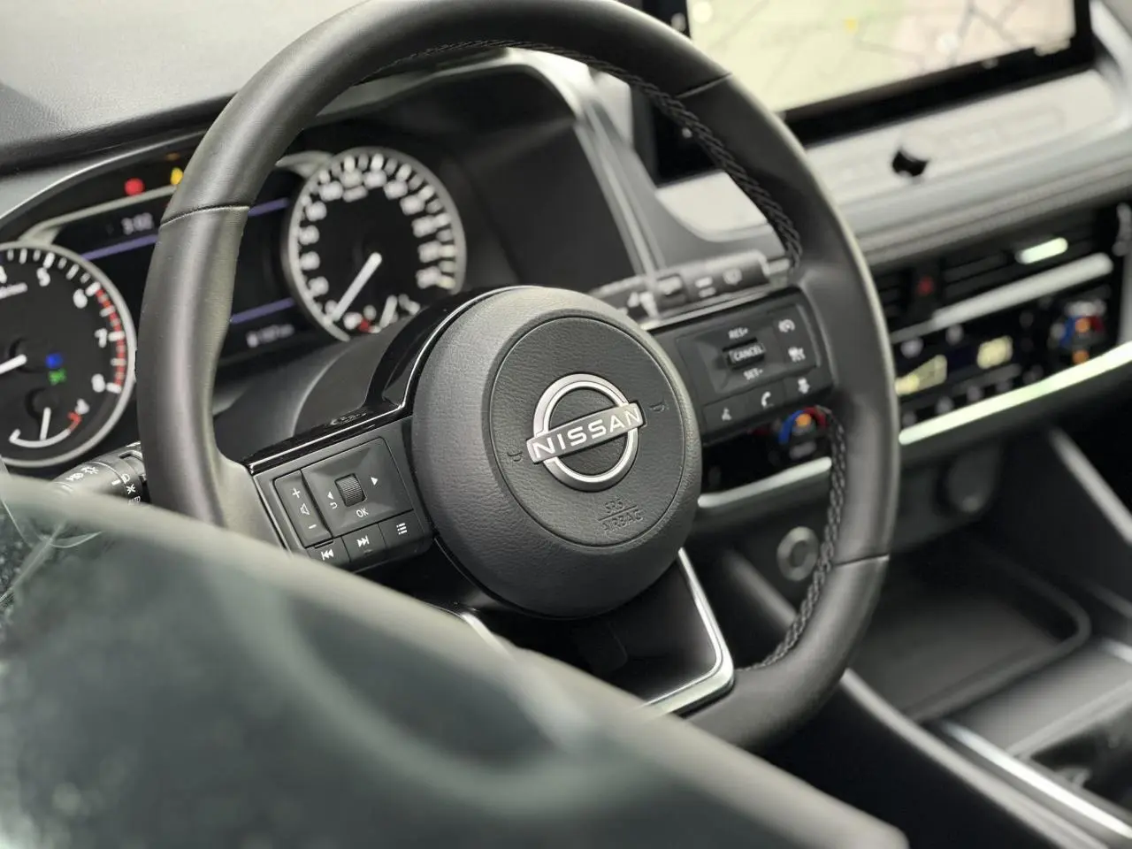 Vue rapprochée du volant noir du Nissan Qashqai 2024 avec commandes intégrées et tableau de bord digital.