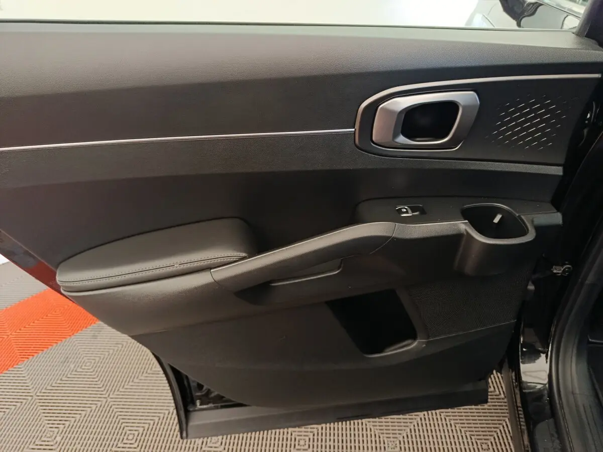 Vue intérieure côté gauche de la porte arrière noire du Kia Sorento 2023 avec poignée argentée et accoudoir rembourré.