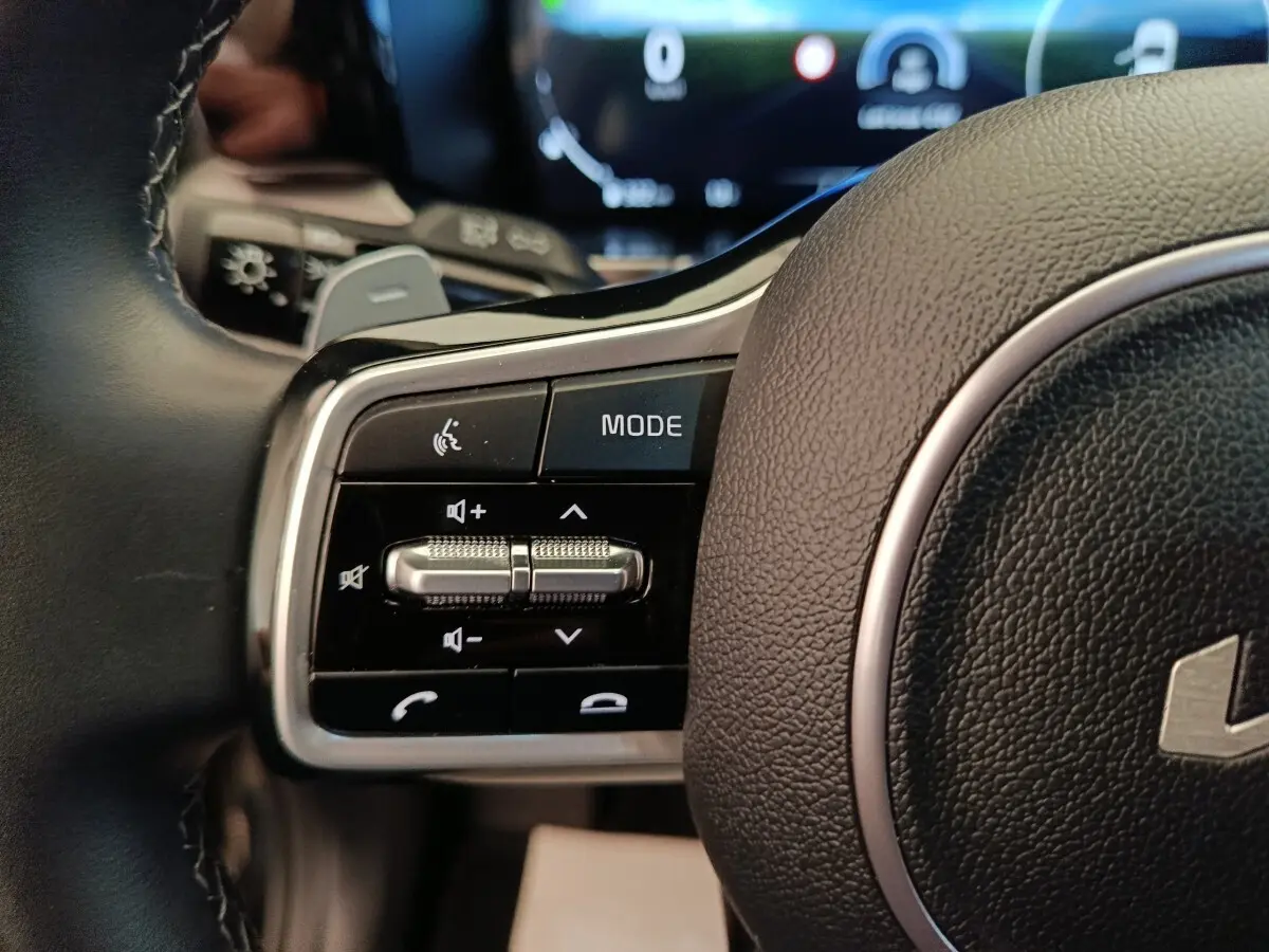 Gros plan sur les commandes gauche du volant cuir noir du KIA Sorento 2023 hybride rechargeable, avec boutons multifonctions.
