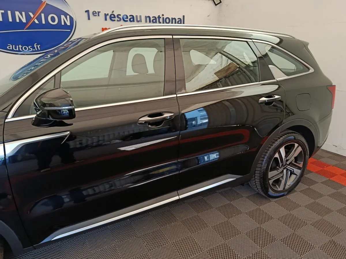 Vue latérale droite d'un KIA Sorento noir 2023 hybride rechargeable, avec jantes alliage et barres de toit chromées.