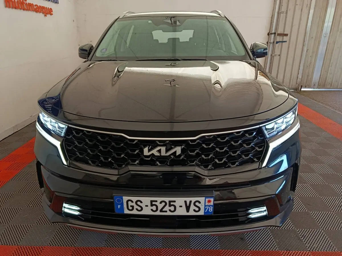 Vue frontale d’un KIA Sorento noir 2023 avec calandre noire et feux LED allumés dans un garage.