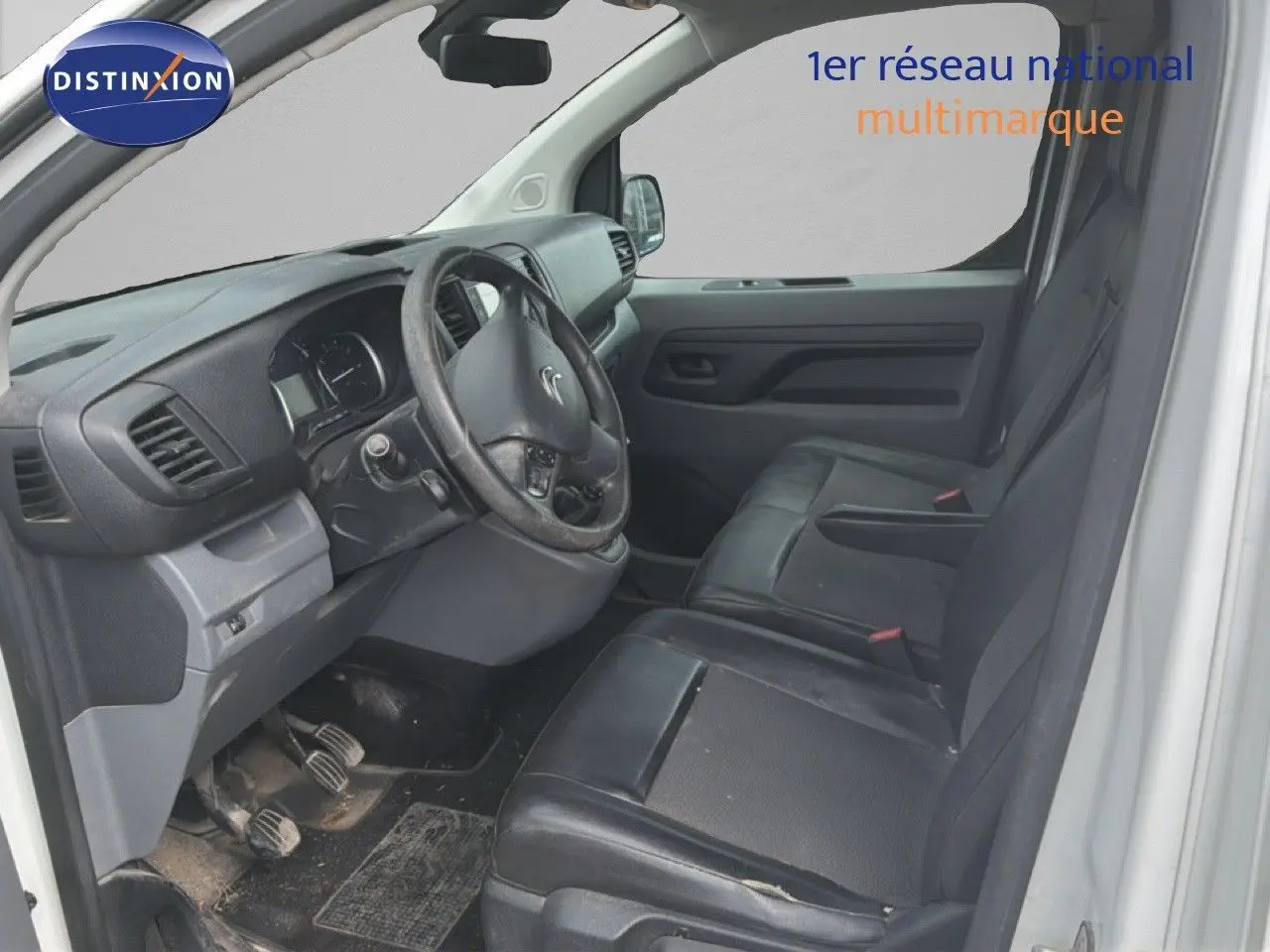 Vue intérieure côté conducteur du Citroën Jumpy blanc, montrant le volant, tableau de bord et sièges noirs en cuir.