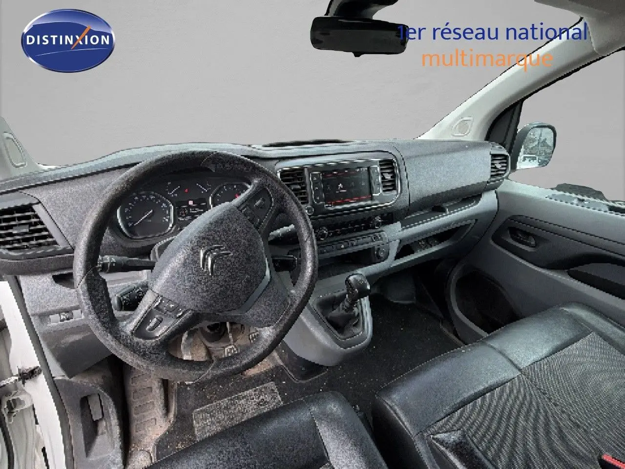 Vue intérieure du poste de conduite du Citroën Jumpy blanc, montrant le volant, tableau de bord et levier de vitesses manuel.