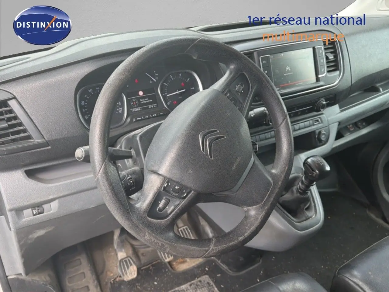 Vue intérieure du poste de conduite du Citroën Jumpy blanc, volant multifonction et levier de vitesses manuel visibles.