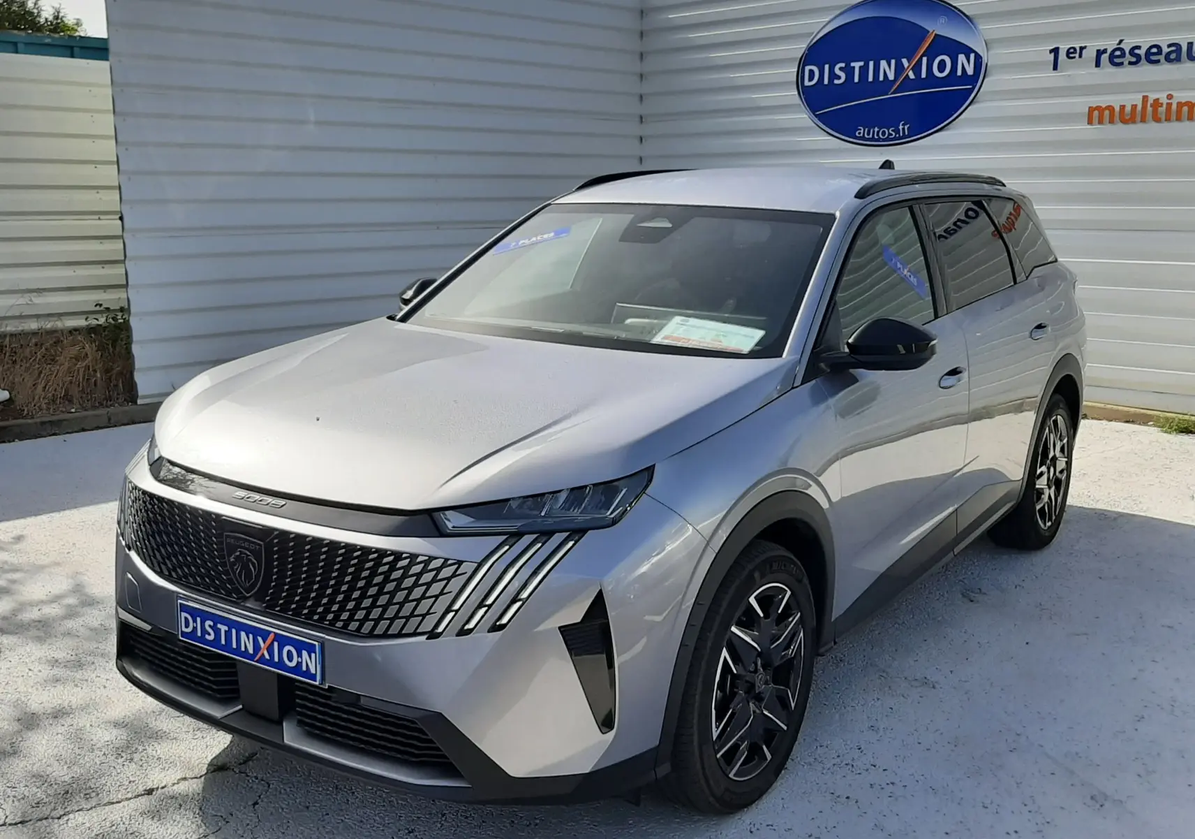 Peugeot 5008 Hybrid gris Artense métal en 3/4 avant droit, avec calandre distinctive et jantes noires bicolores.