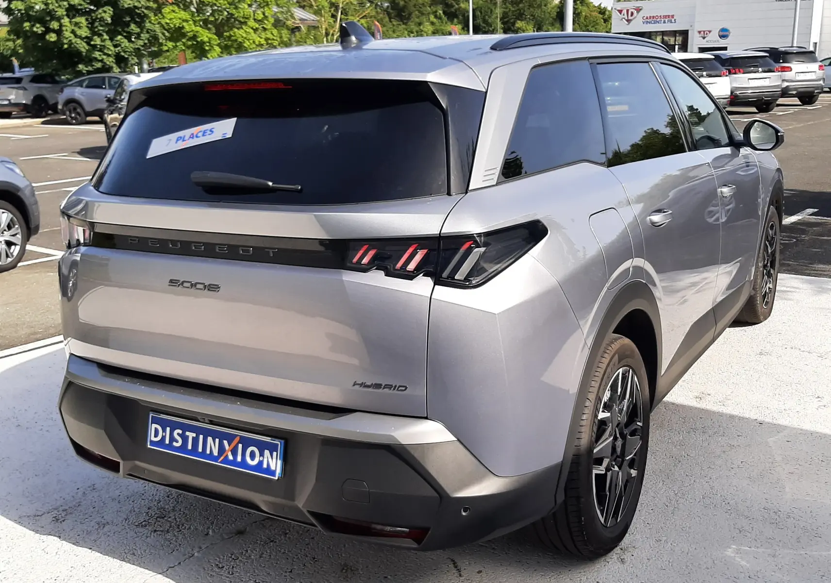 Vue 3/4 arrière droite d’un Peugeot 5008 Hybrid gris Artense métal avec vitres teintées et feux arrière à LED distinctifs.