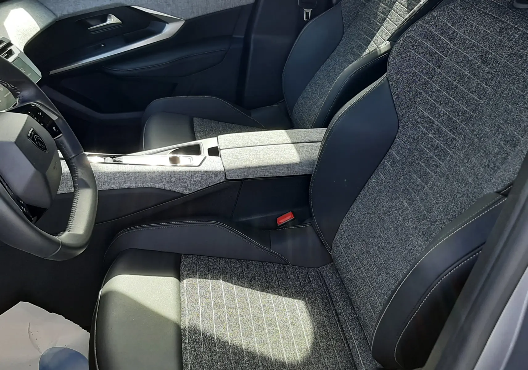 Vue intérieure côté conducteur du Peugeot 5008 Hybrid 2025, sièges tissu gris et cuir noir avec console centrale assortie.