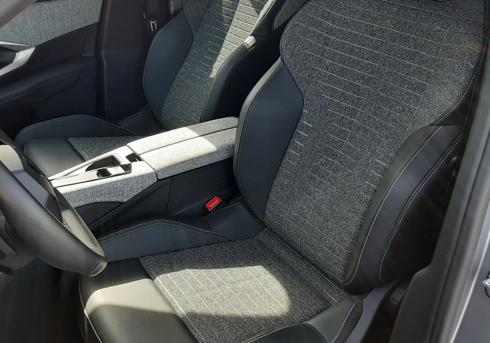Vue intérieure rapprochée des sièges avant gris tissu et cuir noir du Peugeot 5008 Hybrid 2025, avec console centrale assortie.