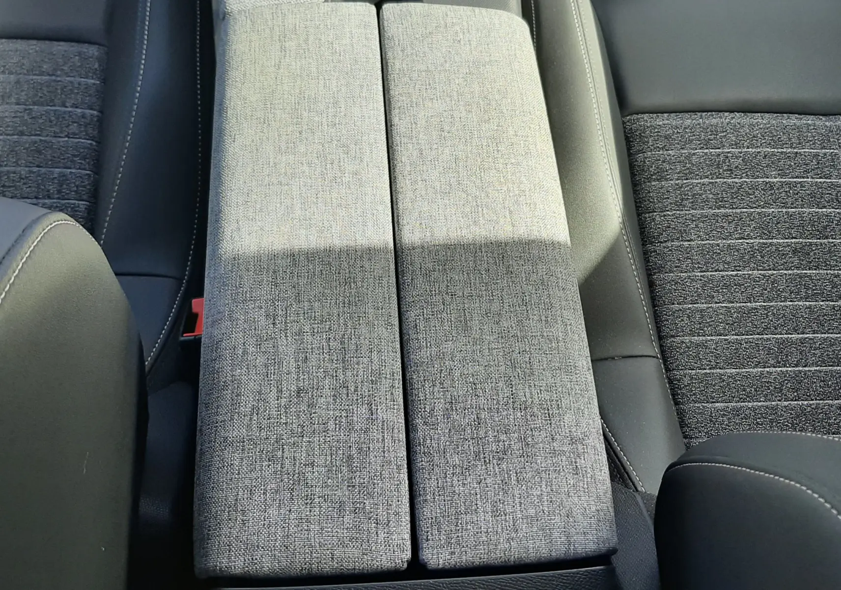 Vue plongeante sur l'accoudoir central gris clair et les sièges tissu gris foncé du Peugeot 5008 Hybrid 2025.