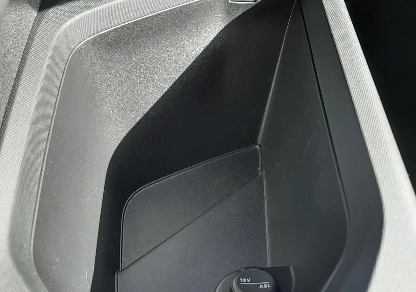 Vue rapprochée du rangement central noir avec prise 12V et port USB dans le Peugeot 5008 Hybrid 2025 gris Artense.