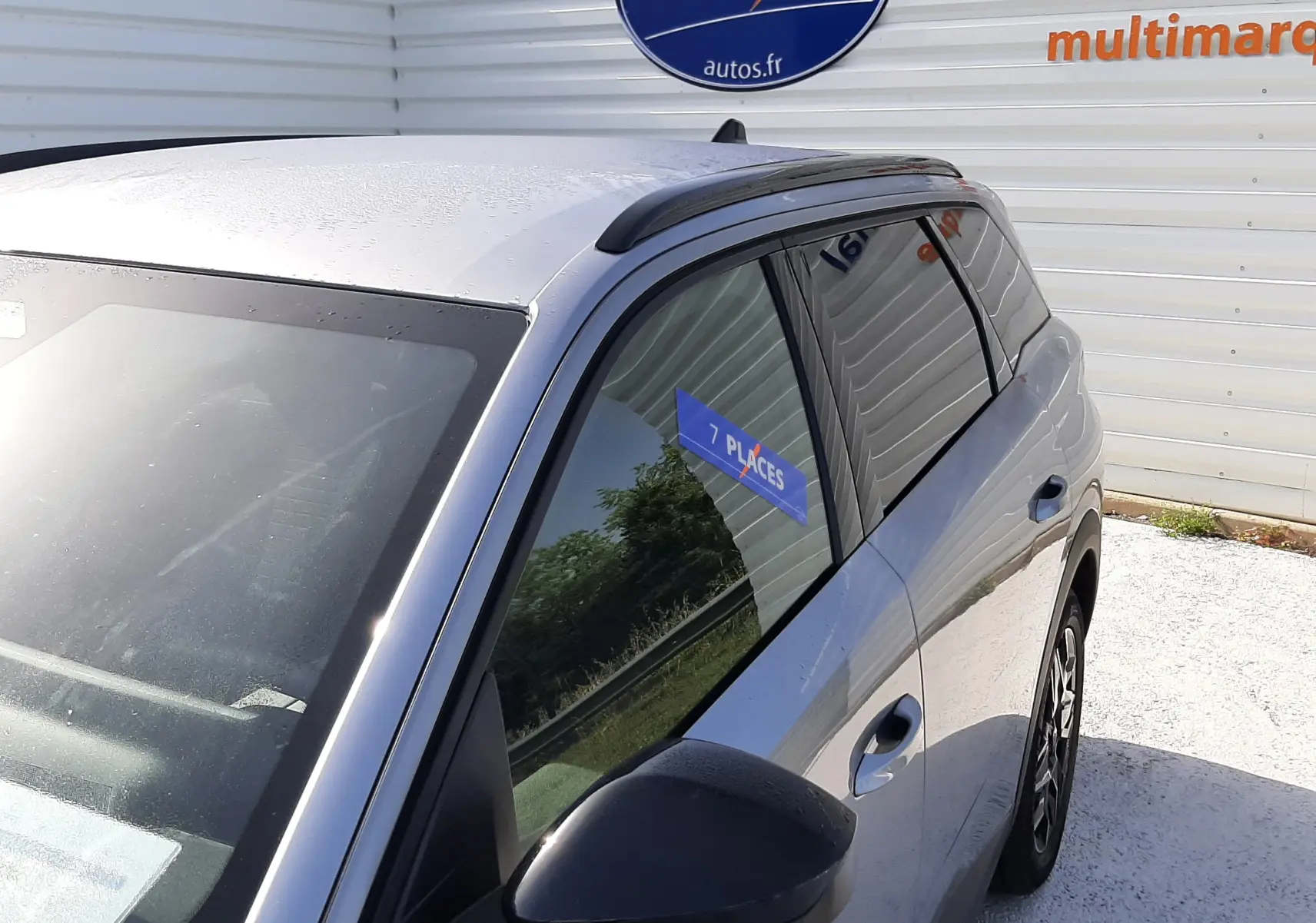 Vue 3/4 avant droit du Peugeot 5008 gris Artense métallisé avec toit panoramique et sticker 7 places sur la vitre arrière.